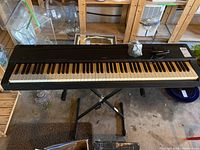 Full view of Yamaha keyboard mounted on X-style stand with pedal and adapter bag on top
