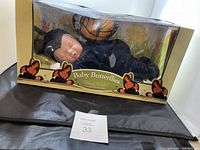 Front and angle views of the Anne Geddes Baby Butterflies doll in its box, showing the doll dressed in a black butterfly costume and the packaging with butterfly illustrations and some visible box damage.