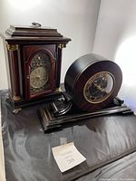 Photo showing both vertical and circular Bombay clocks against white background on black surface