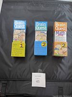 Photo shows three Brain Quest decks in boxes on a black surface with MaxSold bid card 45.