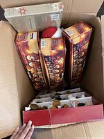 Photo showing boxed mini water globe train sets, a Santa decoration hat, and other boxed holiday items inside a cardboard box.