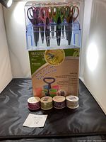 Photo showing multiple pairs of Fiskars scissors in a clear plastic caddy with brand label, and five rolls of decorative craft tape in front of caddy.