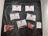 Photo of five Canadian Red Cross pocket-sized first aid kits including sealed packages of medical supplies and red coiled bulbs.