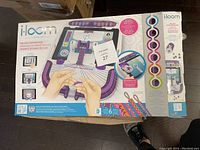Photo of iLoom Deluxe Starter Pack box showing the weaving kit designed for use with iPad and selected tablets. Box shows illustrations of loom parts and weaving process.