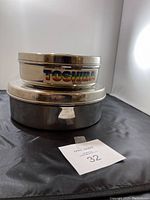 Side view of two stacked stainless steel spice trays, showing metallic finish and Toshiba logo on top lid.