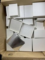 Multiple white rectangular jewelry gift boxes stacked in a cardboard box. Some lids removed to show inside.