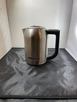 Front view of the stainless steel electric kettle with black handle, showing the KitchenAid logo on the front.