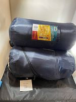 Two blue nylon bags containing sleeping bags stacked, showing label with temperature rating 8-10 degrees Celsius.
