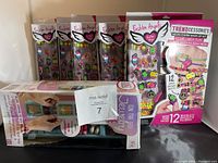 Photo showing five boxed Fashion Angels Neon Charm Mash-Up Kits and one boxed jewelry storage case on a black surface against a wall.