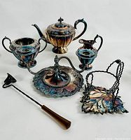 Overall view of antique silver plated teapot, two-handled sugar bowl, water pitcher, candle snuffer, candle holder, and leaf tray.