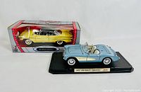 Photo showing both die-cast models: a light blue 1957 Chevrolet Corvette on a display base and the boxed yellow 1961 Desoto Adventure model.