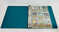 Open three-ring binder with nine-pocket plastic page showing Magic: The Gathering cards, mostly green cards.