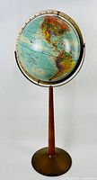 Full view of the midcentury Replogle globe on a tall teak stand with metal round base.