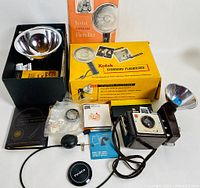 Full lot showing Kodak Brownie camera with attached flash holder, Kodak Standard Flasholder box and manual, various camera accessories, film packets, lens cap, and case.