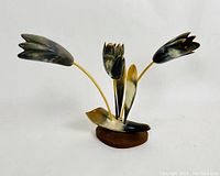 Front view of carved floral arrangement showing three flowers with dark and light color detailing on petals, set on yellow stems mounted on an oval wooden base.