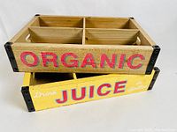 Photo showing two wooden advertising crates stacked, one yellow with 'JUICE' text, one natural wood with 'ORGANIC' text.