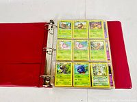 Open red 3-ring binder displaying first page of Pokemon cards in protective sleeves, featuring characters such as Zigzagoon, Lombre, Clefairy, Tentacool