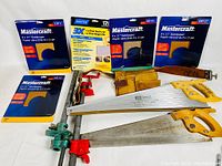 Five packs of unopened Mastercraft sandpaper in various grit sizes along with hand saws and clamps arranged together.