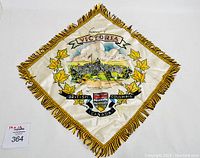 Front view of the vintage souvenir pillow cover showing the printed image of Victoria Parliament Buildings and decorative fringes.