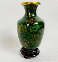 Front view of the emerald green cloisonné floral vase on its wooden base, showing the vibrant floral pattern and gold rim.