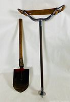 Front view of wood, leather, and metal perch stick next to vintage latrine shovel showing their overall shape and condition.