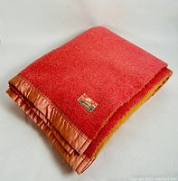 Folded pink wool blanket with satin ruffled trim and visible Ottawa Valley Woollens label on one side.