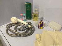 Photo showing handheld shower head and hose, Elizabeth Taylor perfume in box, Eau de Rochas perfume bottle, soap dish, yellow and purple soap risers, and bar of soap.