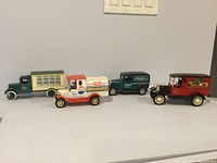 Front angle view showing 4 of the 5 collectible die-cast truck banks lined up on a flat surface.