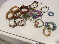 Overview photo of assorted costume bracelets including wooden bangles, beaded bracelets, charm bracelets, and woven bracelets laid out on a white surface.