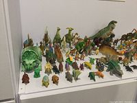 Wide view of dinosaur and prehistoric animal models displayed on a white surface, showing a variety of species and colors.
