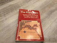 The Rishonim book with red cover showing a geographical map and text describing biographies of early rabbis.