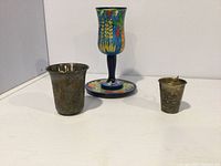 Set of three Kiddush cups: two silver and one colorful hand-painted Israeli cup