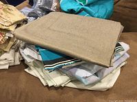 Folded beige fabric on top of blue striped and solid color fabrics on a brown surface