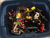 Blue plastic storage bin filled with various small model cars and trucks in multiple colors and styles.