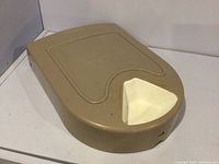 Top angled view of light brown rectangular plastic pet feeder with white feeding dish opening and slight surface marks.