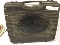 Black hard plastic carry case for portable gas stove, showing handle, ribbed design and embossed text.