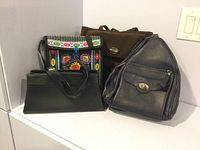 Six purses grouped together showing variety of colors and styles including floral embroidered and dark blue leather bag.