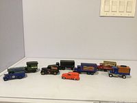 Seven assorted die cast model postal and delivery trucks displayed in a row showing variety of designs and colors, including blue, green, black, orange, and purple.