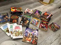 Wide shot of multiple stacks and piles of Star Wars books scattered on a floor, showing variety of book sizes, covers, and some titles like 'The Clone Wars', 'Fortune Wookiee', 'Jedi Academy', and more.
