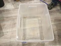 Top view inside of a large clear plastic storage bin showing circular feet and some dirt inside.