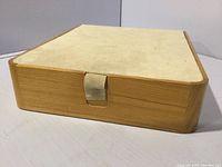 Top angled view of rectangular wooden jewelry box with cream fabric top and fabric pull tab, showing some dirt and wear.