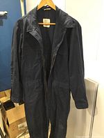 Front view of a dark navy US Navy coverall hanging on a hanger showing the collar, sleeves, and double zipper partially unzipped.