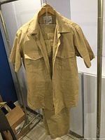 Tan US Navy cotton short-sleeve working shirt with two large chest pockets and matching pants hanging on rack.