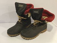 Pair of Storm By Cougar women's winter boots viewed from front with inner red knit lining exposed, laces tied, and branding patch on tongue visible.