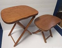 Two vintage NEVCO wooden folding stools, one larger and one smaller, on white background showing front view and leg structure.
