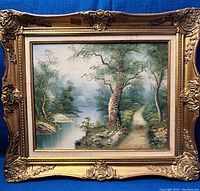 Full view of framed landscape painting showing river, trees, and path with ornate gold frame.