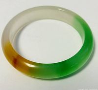 Top close-up of the jade bangle bracelet showing the smooth polished surface and multi-colored jade stone including green and brown areas.