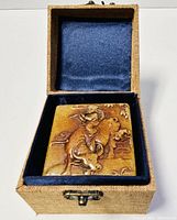 Raised carved Shoushan trinket box inside blue-felt lined beige cloth-covered box, top view showing detailed carving of figure on water buffalo.
