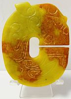 Front view of hand carved Chinese jade amulet showing detailed carvings and warm yellow-brown tone.