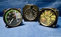 Front view photo showing three vintage aircraft instruments; tachometer, compass, and fuel indicator with detailed dials and markings.